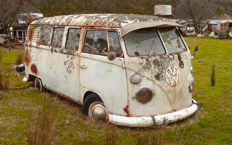 old rusted split-window VW bus in a field